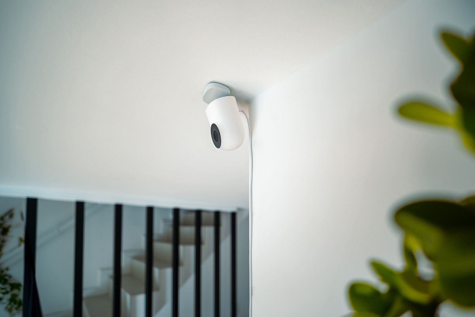 Une caméra de surveillance blanche fixée au mur en haut d'un escalier, dans une maison